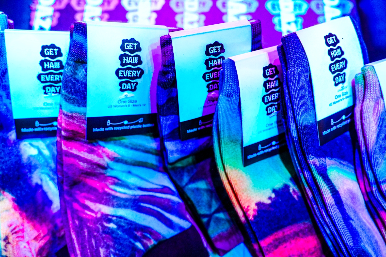 Colorful “Get Haiii Every Day” socks displayed under neon rainbow lighting from the Haiiileen x Tribe Socks collection.
